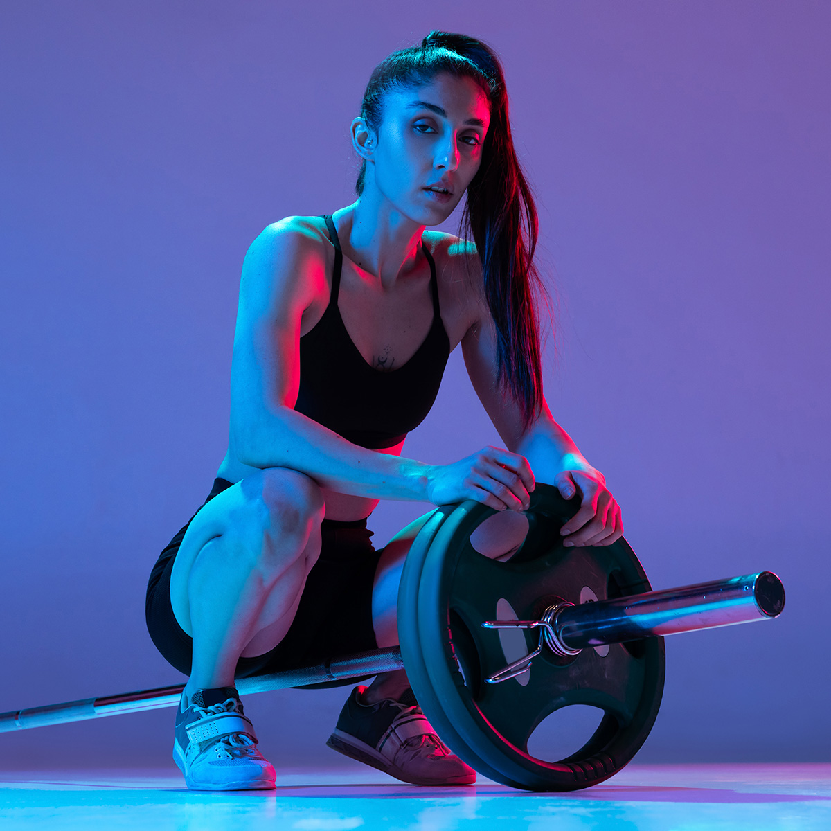 portrait-of-muscled-woman-training-with-a-barbell-isolated-on-purple-background-in-neon-light